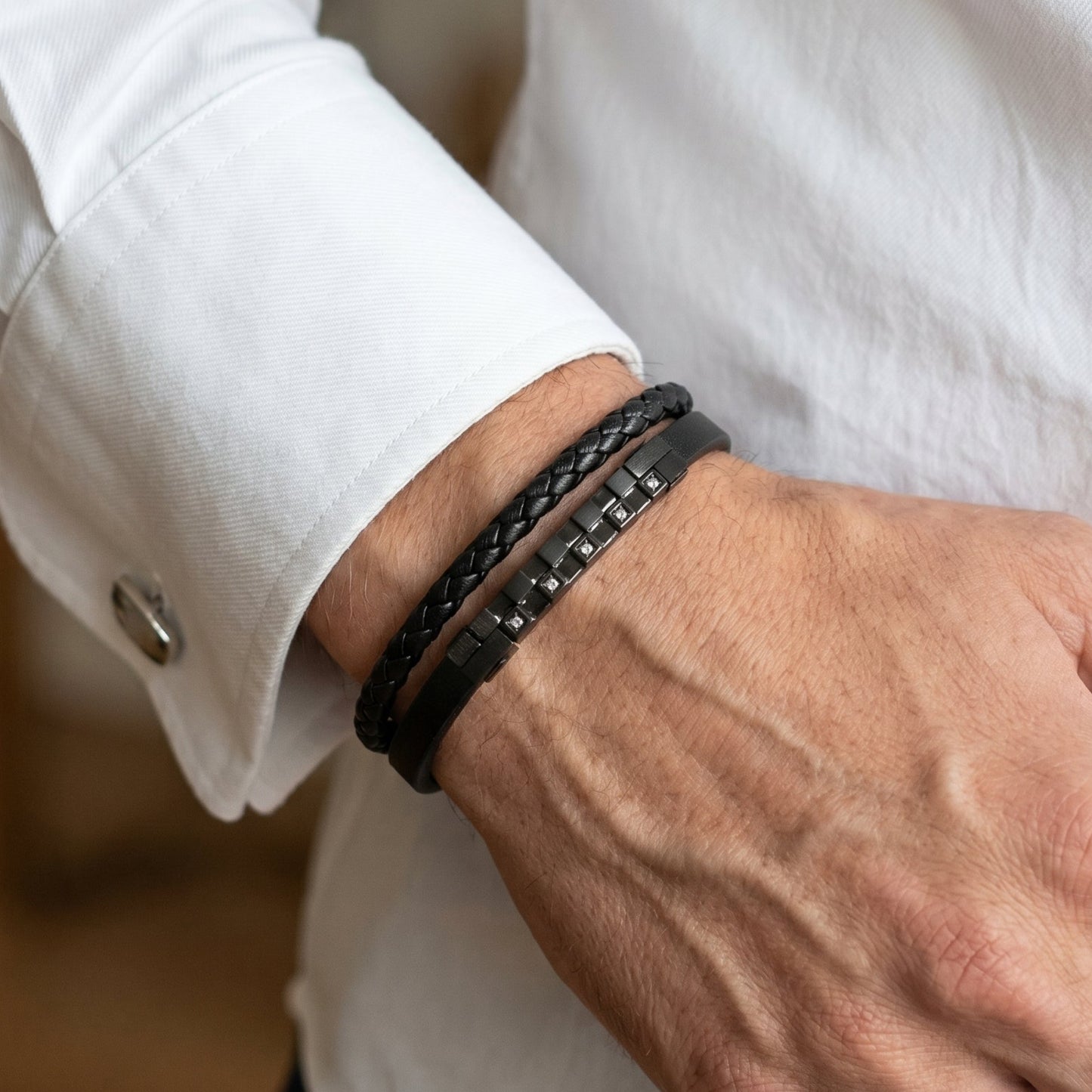 Men's black leather bracelet on wrist, layered leather bands with dark zircon square studs.