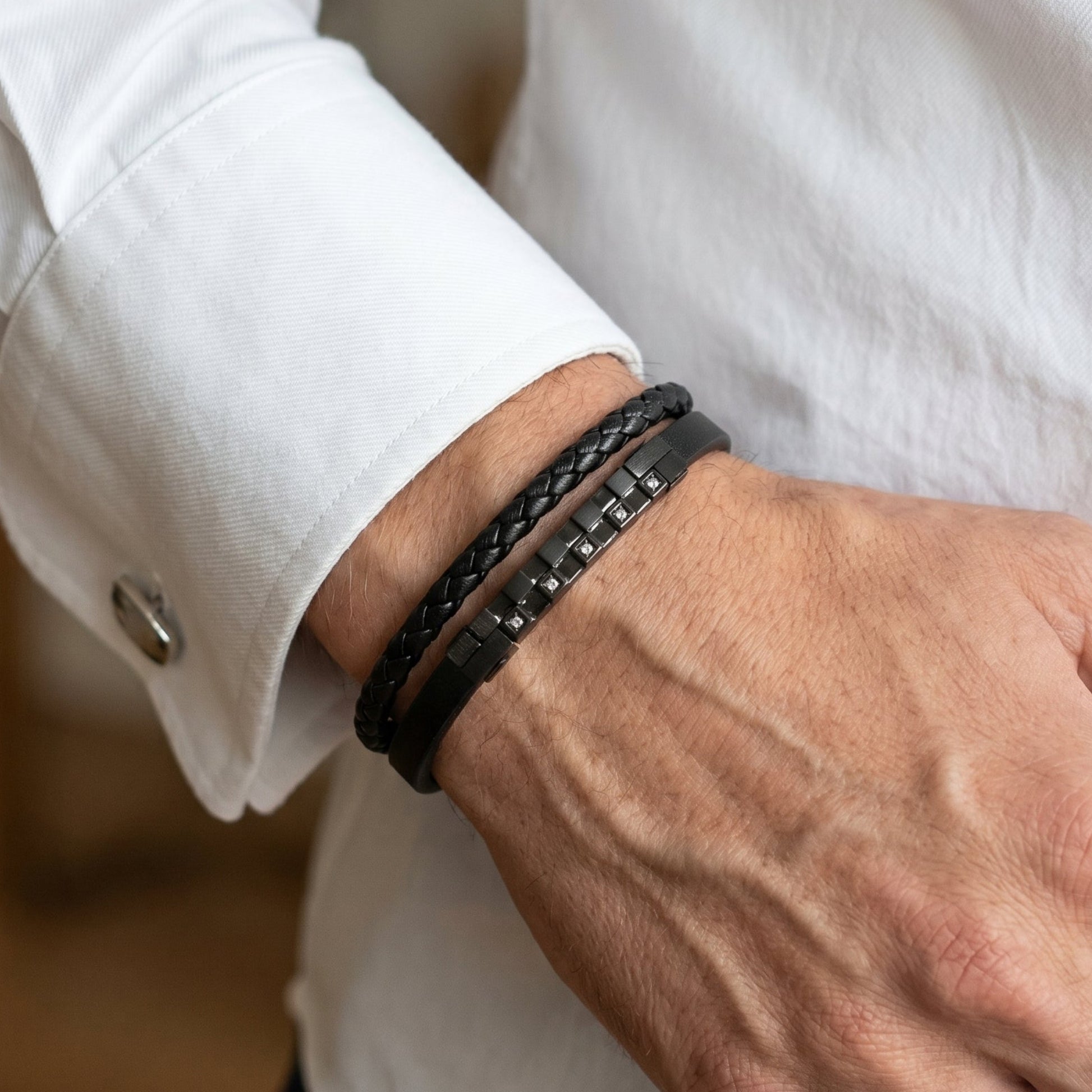 Men's black leather bracelet on wrist, layered leather bands with dark zircon square studs.