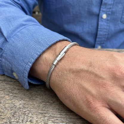 Silver stainless steel bracelet with a magnetic clasp, worn on a wrist, featuring a sleek cable design.