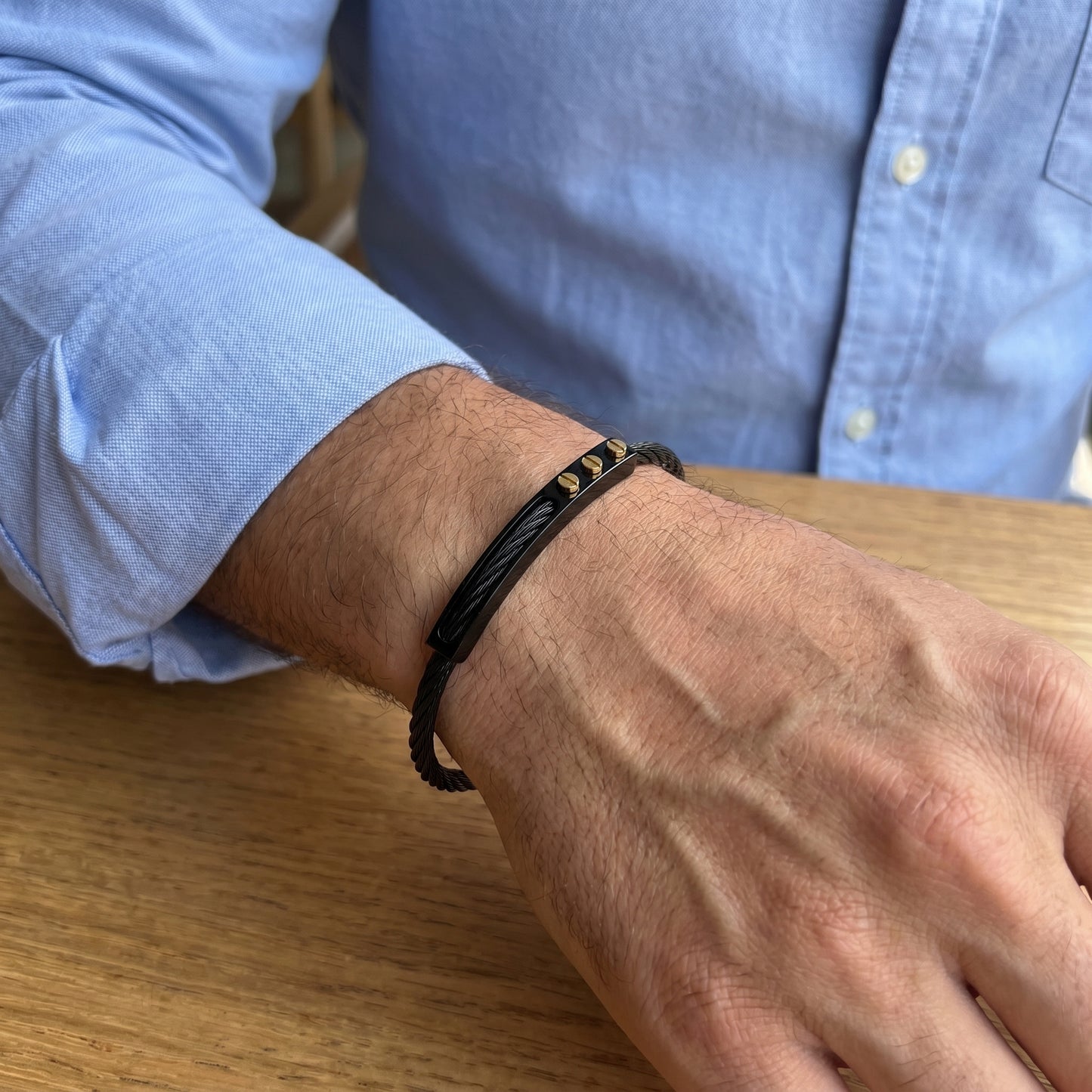 A man wearing a black bracelet on a wooden surface with a blue shirt.