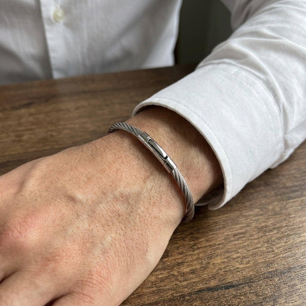 Silver stainless steel bracelet with a magnetic clasp, worn on a man's wrist, set against a wooden surface.