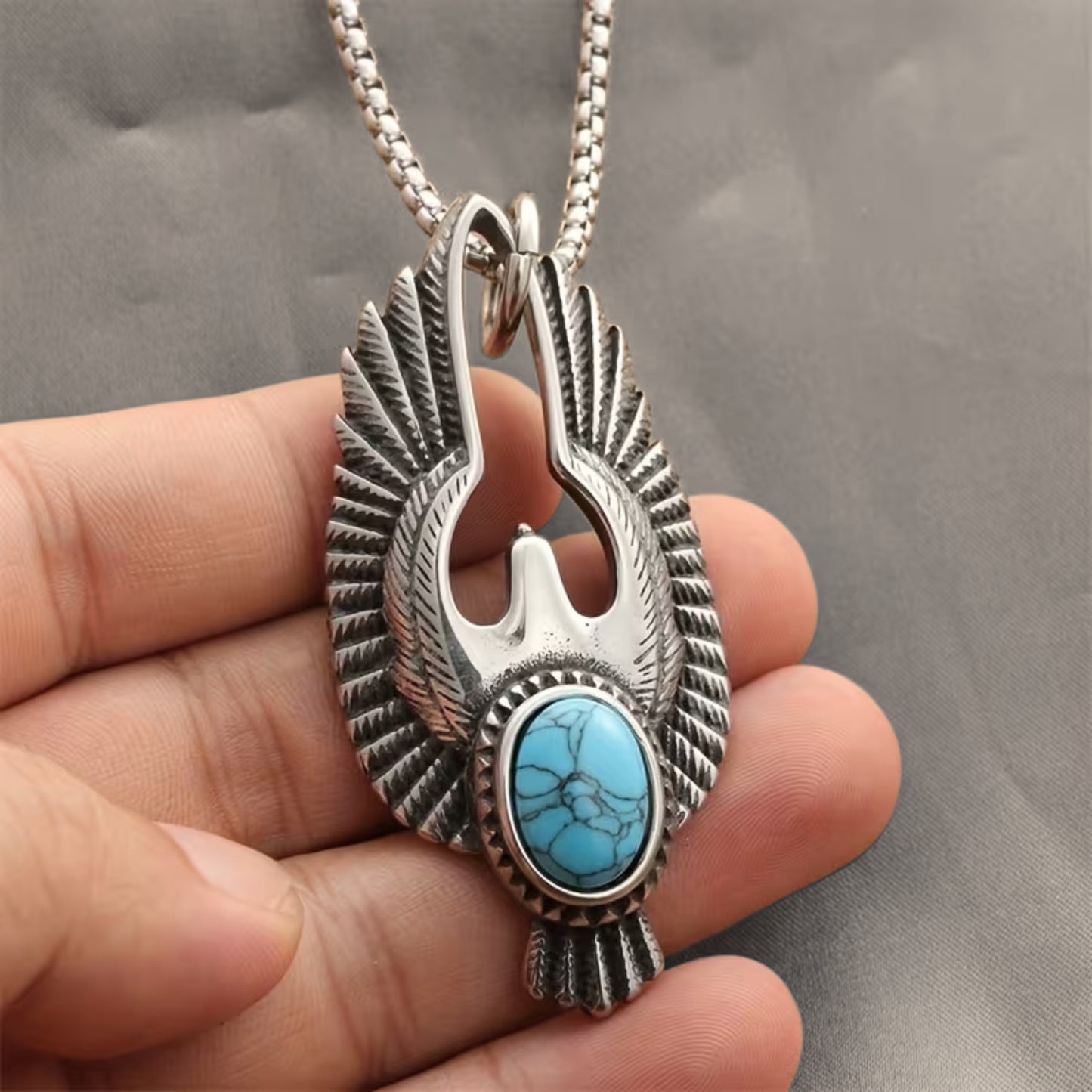 Silver eagle pendant with turquoise cabochon stone, held by fingers with chain loop
