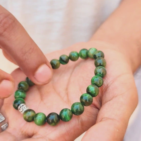 Green tiger's eye bracelet on wrist with silver-toned, engraved clasp centerpiece.