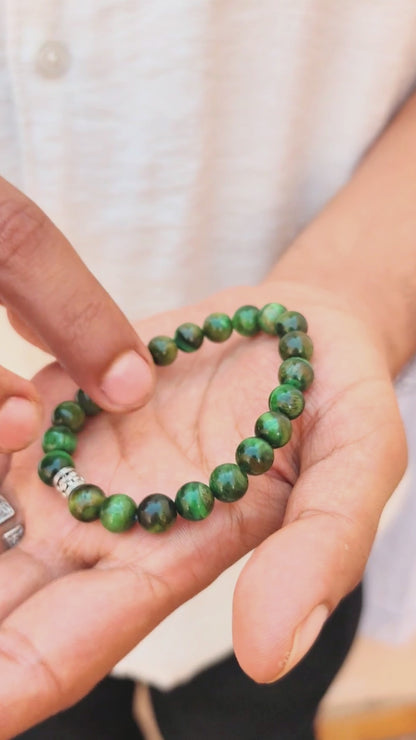 Green tiger's eye bracelet on wrist with silver-toned, engraved clasp centerpiece.