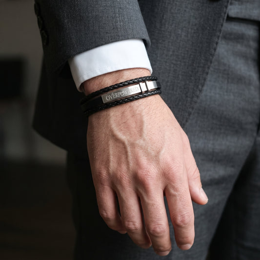 Men's black leather bracelet on wrist, adjustable strap with 'OVERPOWERED' lettering