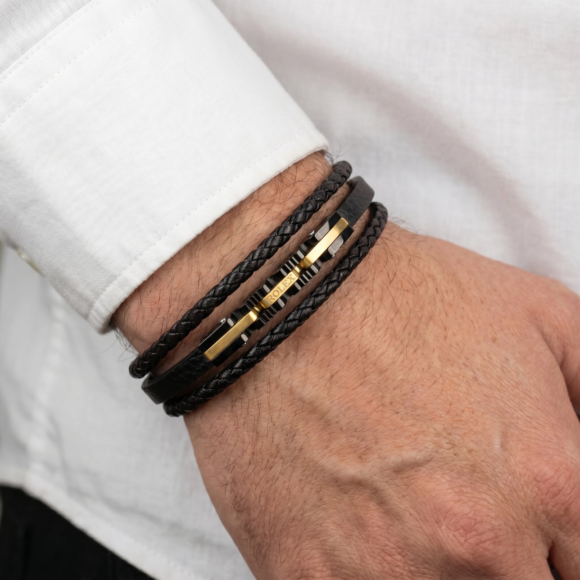 Black braided leather bracelet on wrist, multiple wraps with gold-tone accent bars