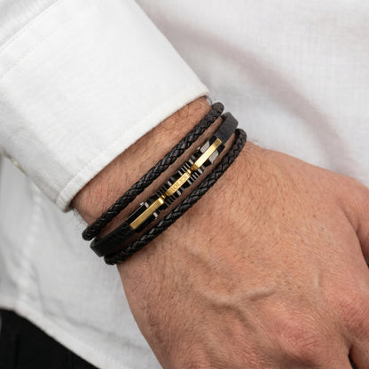 Black braided leather bracelet on wrist, multiple wraps with gold-tone accent bars