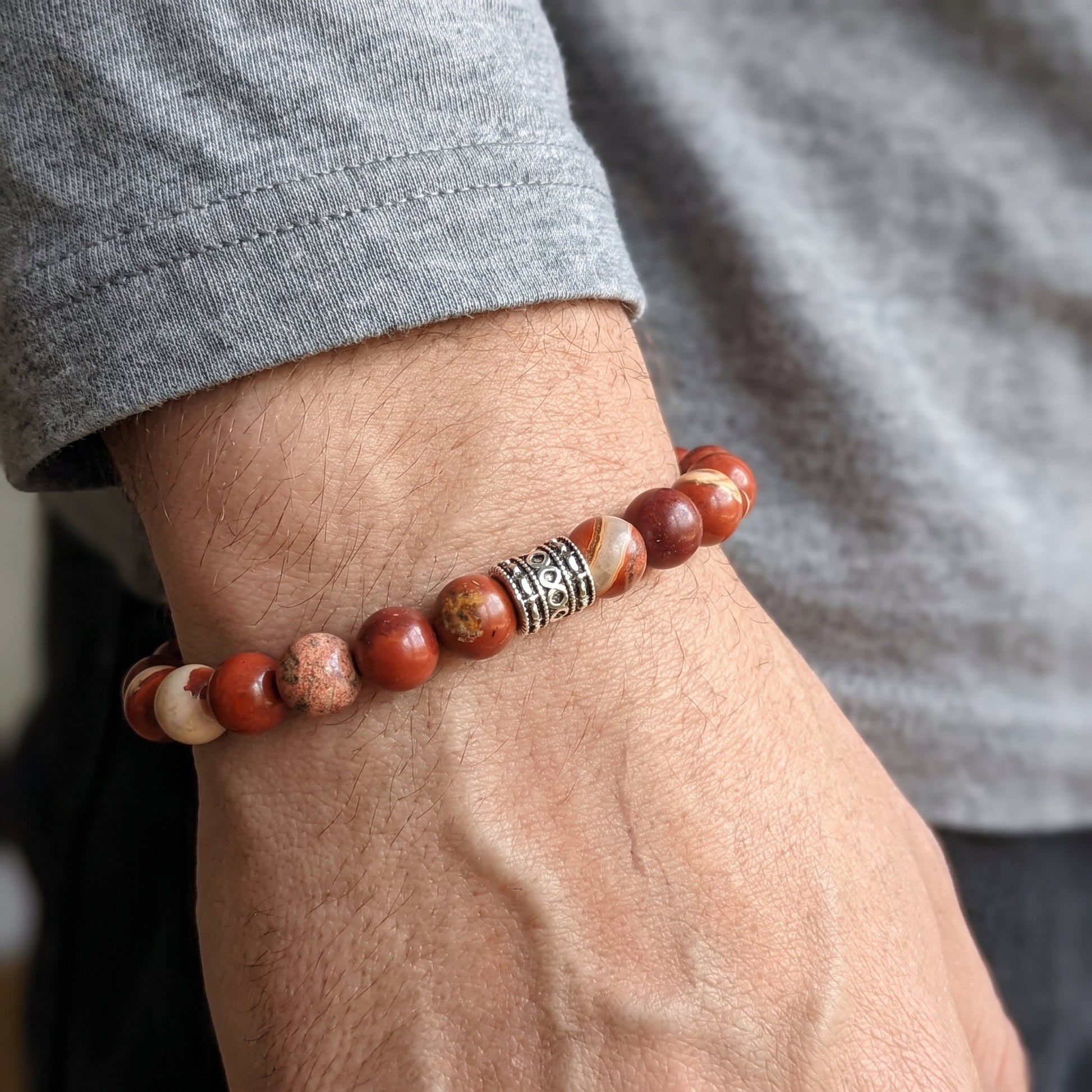 Red jasper stone bracelet worn on wrist, round beads with silver-tone patterned clasp