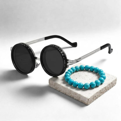 Men's sunglasses with round black lenses and silver frames, paired with a turquoise stone bracelet on a light gray surface.