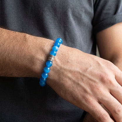 Blue agate bead bracelet worn on wrist with engraved dark metal centerpiece.