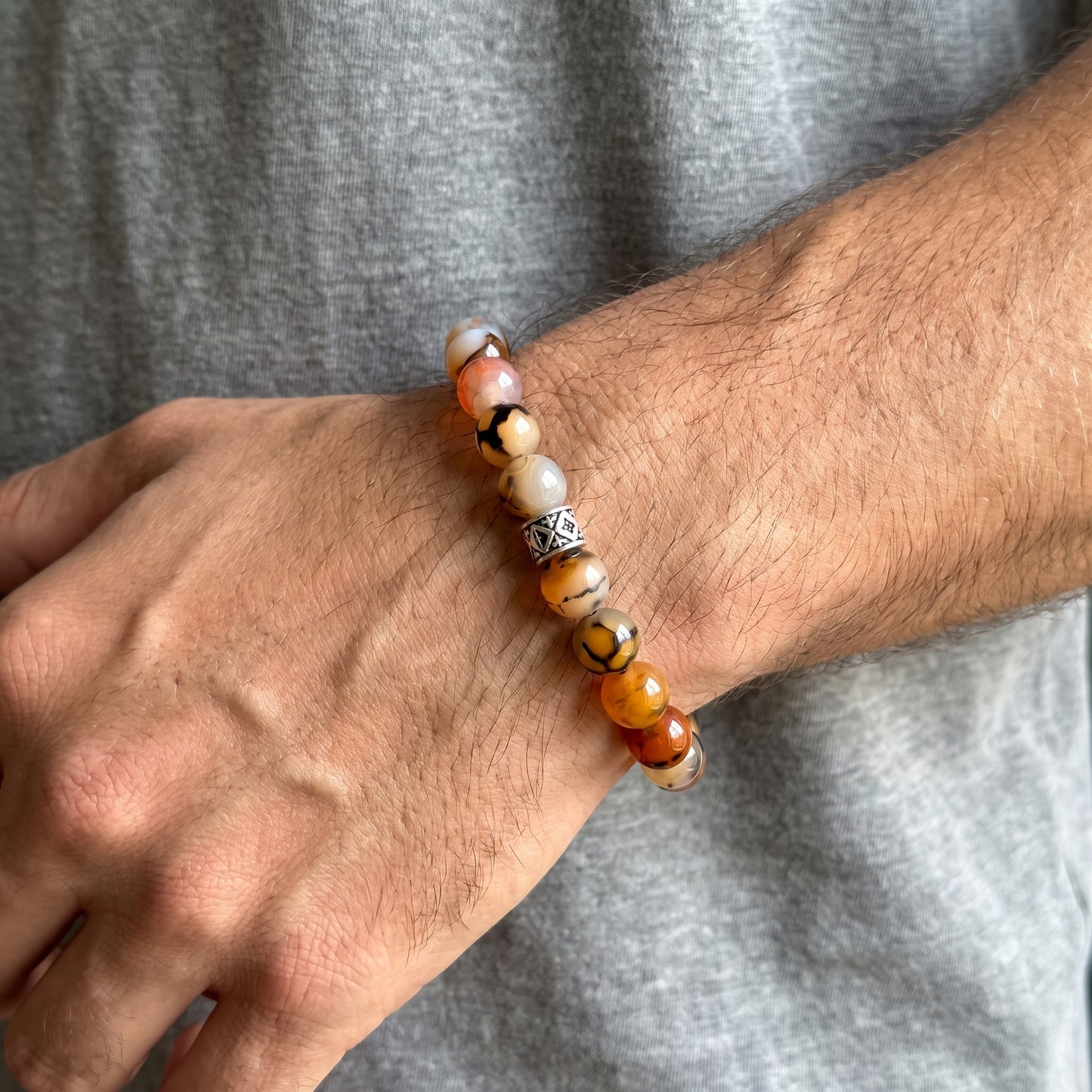 Natural agate bracelet on wrist with orange, tan, black, and white beads and silver geometric link