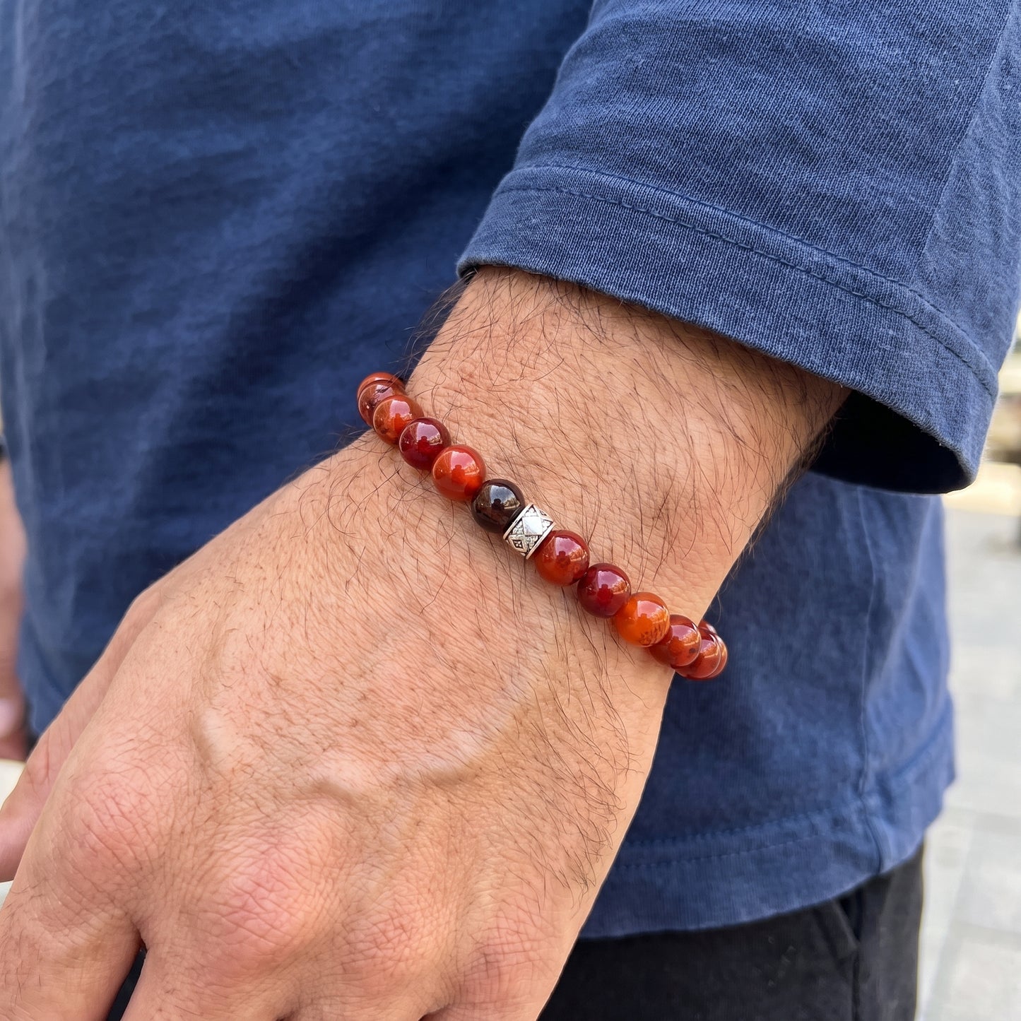 Red agate beaded bracelet on men's wrist with dark beads and silver geometric charm