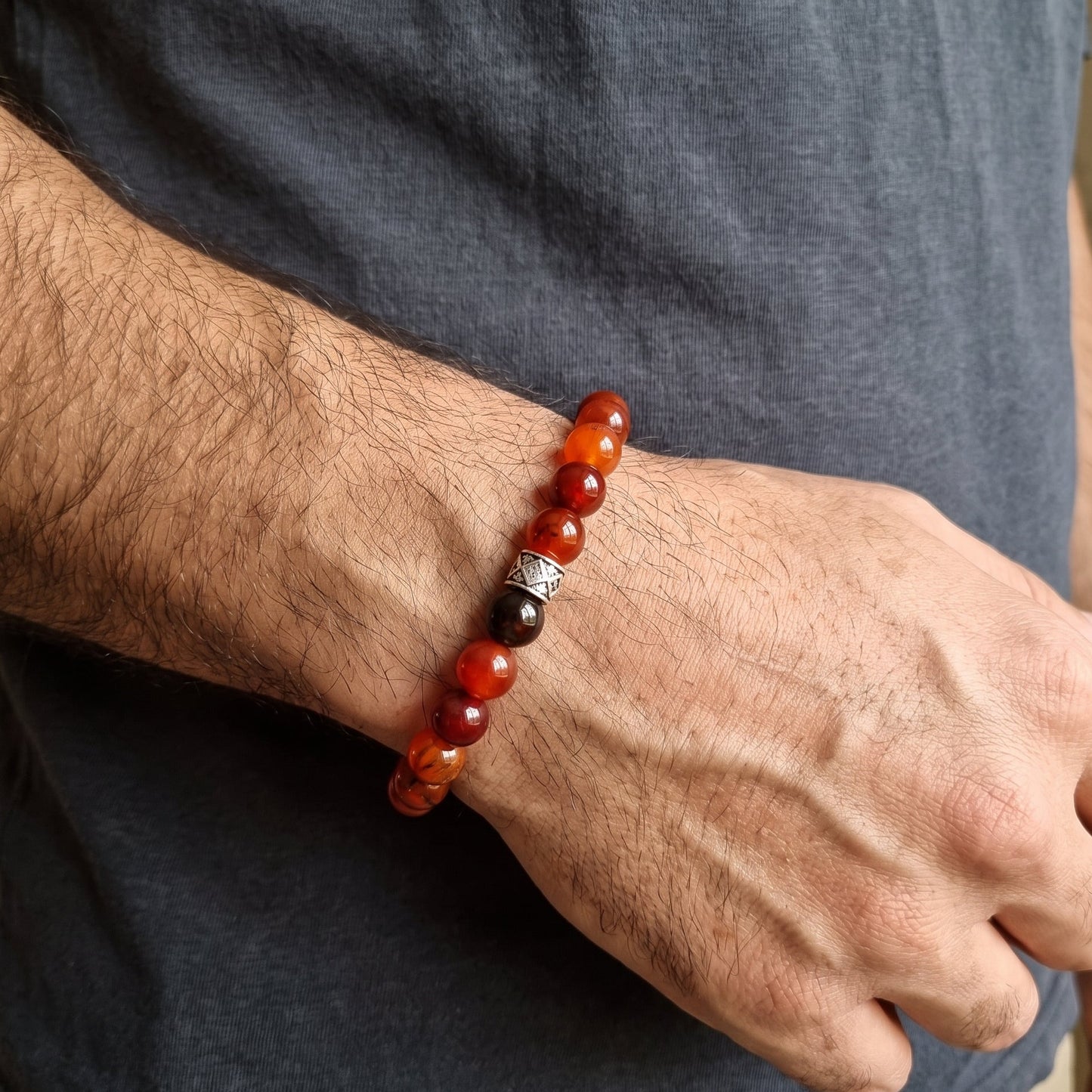 Men's wrist bracelet of red agate beads with dark accents and silver geometric charm
