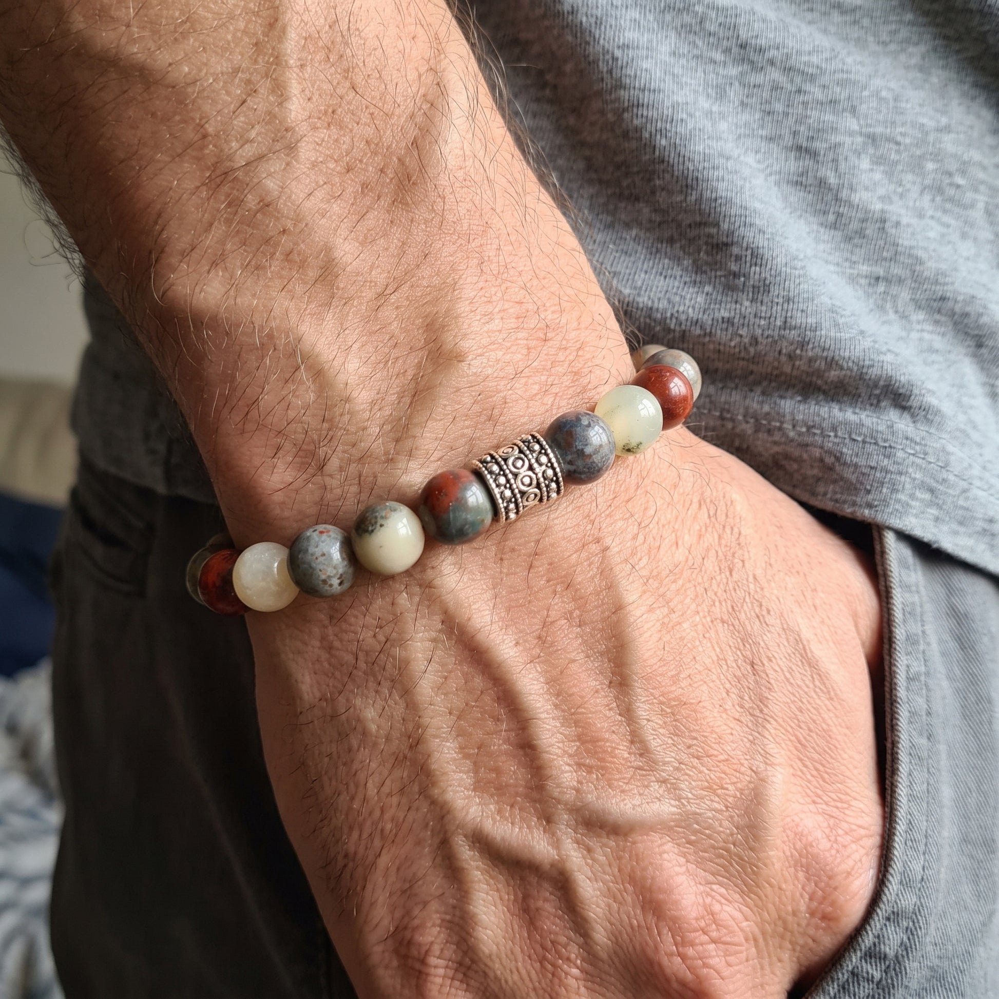 Men's natural stone bracelet worn on wrist, featuring red accents, cream and gray beads, metal spacer