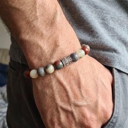 Men's natural stone bracelet worn on wrist, featuring red accents, cream and gray beads, metal spacer