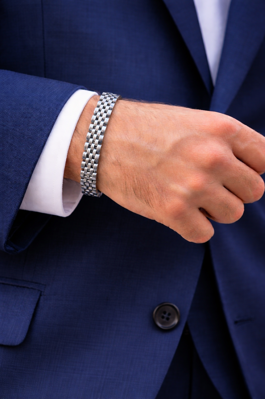 Silver-tone checker-pattern bracelet on a man's wrist with blue suit sleeve