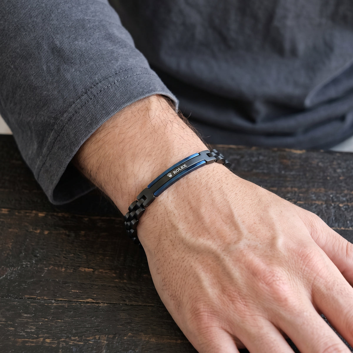 Adjustable black and blue ID link stainless bracelet on forearm resting on wood