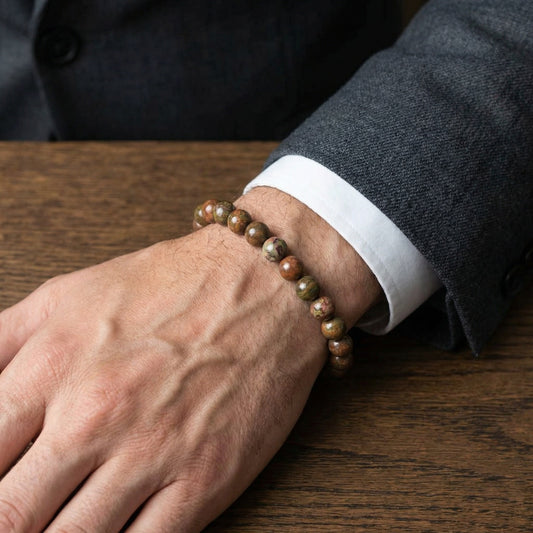 Men's Earthbound Sovereignty Bundle G-5 G-6 stone bracelets on a wrist, styled with a suit, resting on a wooden surface.