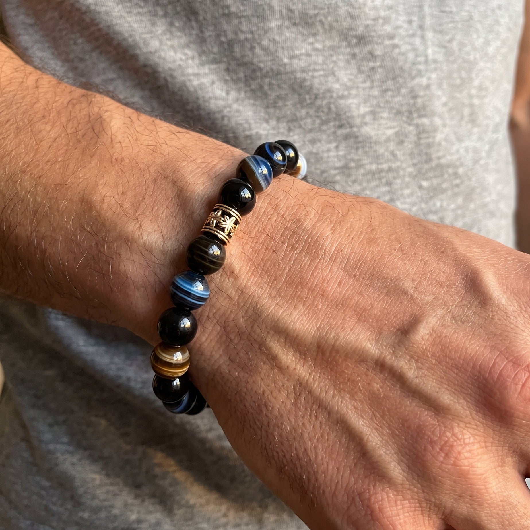 Men's agate bracelet on wrist with dark blue and black beads plus brown striped accents