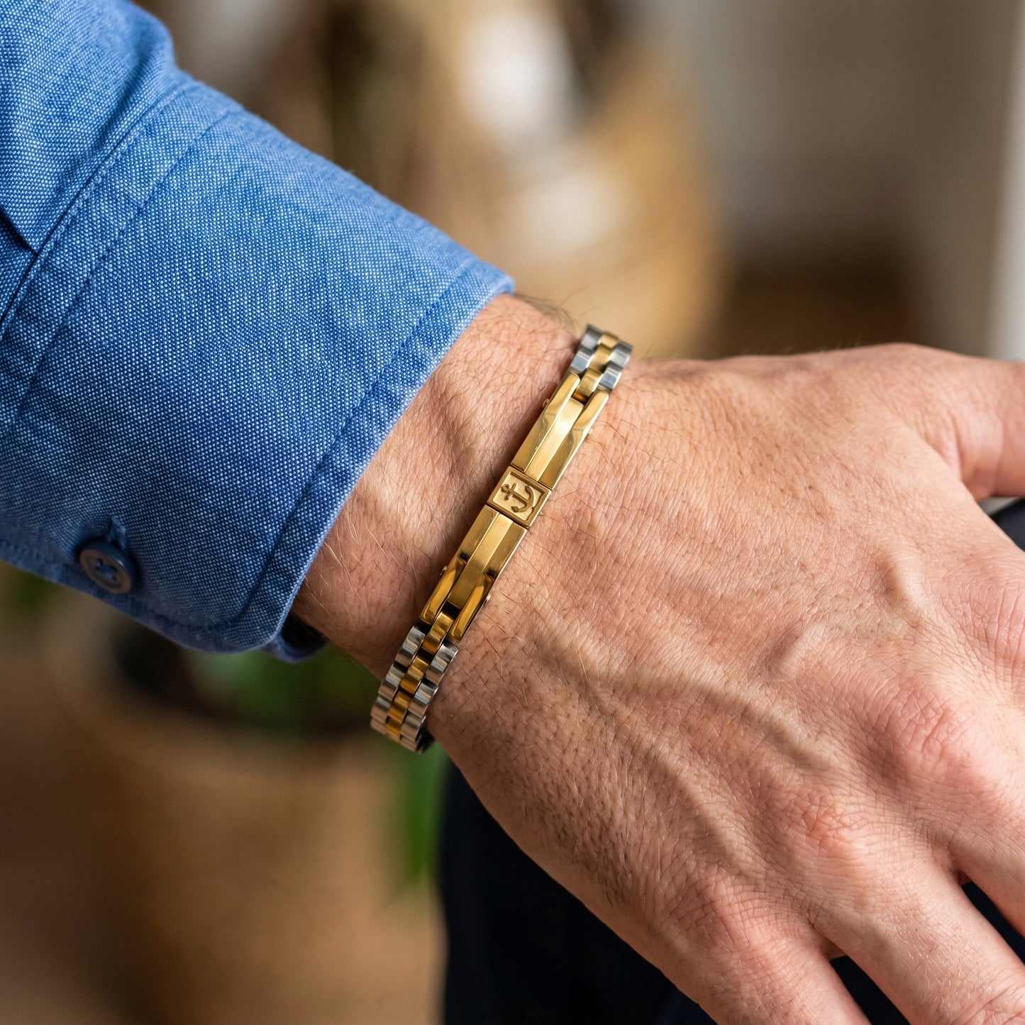 Two-tone anchor bracelet on wrist with gold center bar and silver links, worn with denim cuff