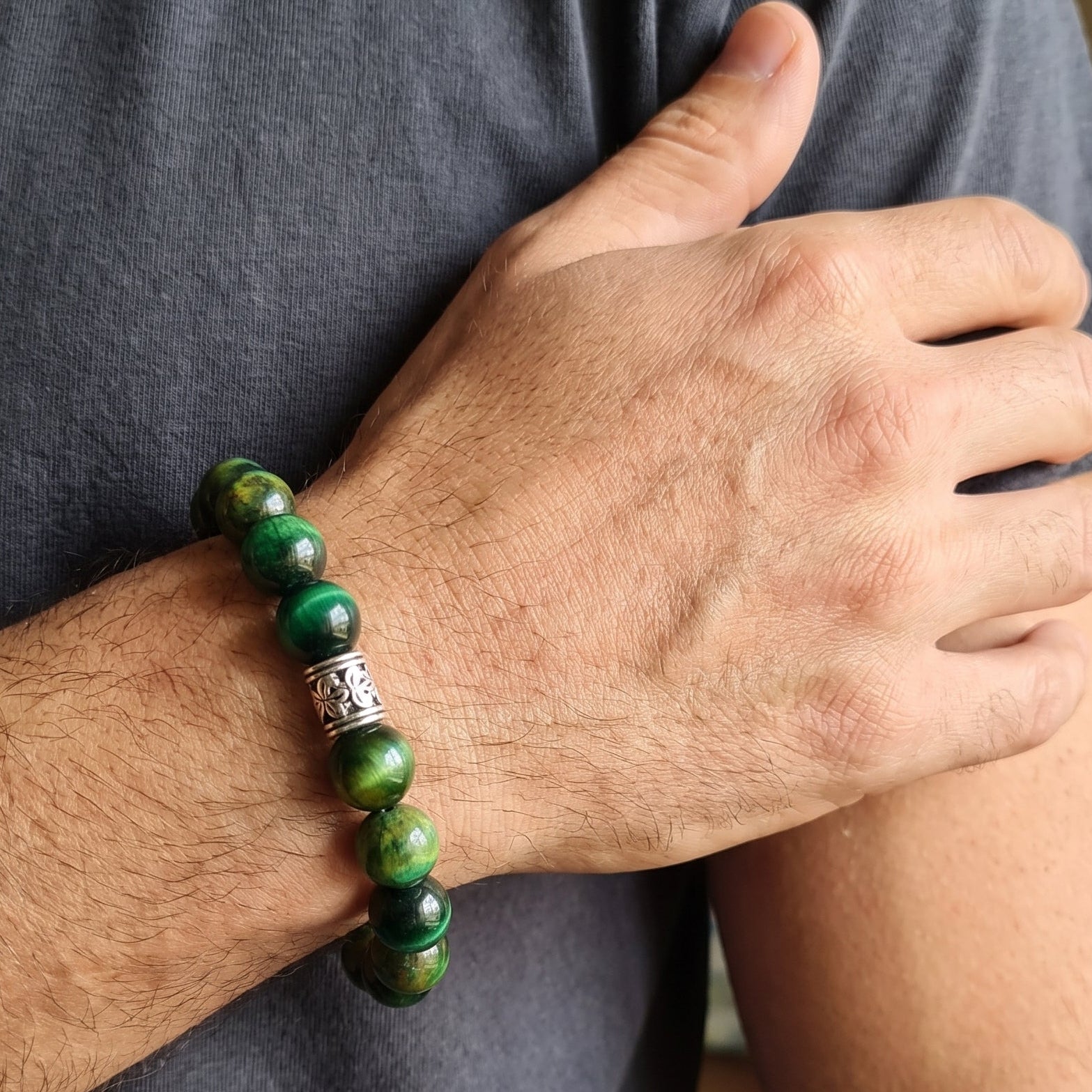 Green tiger's eye bead bracelet on male wrist with silver-toned clasp detail.