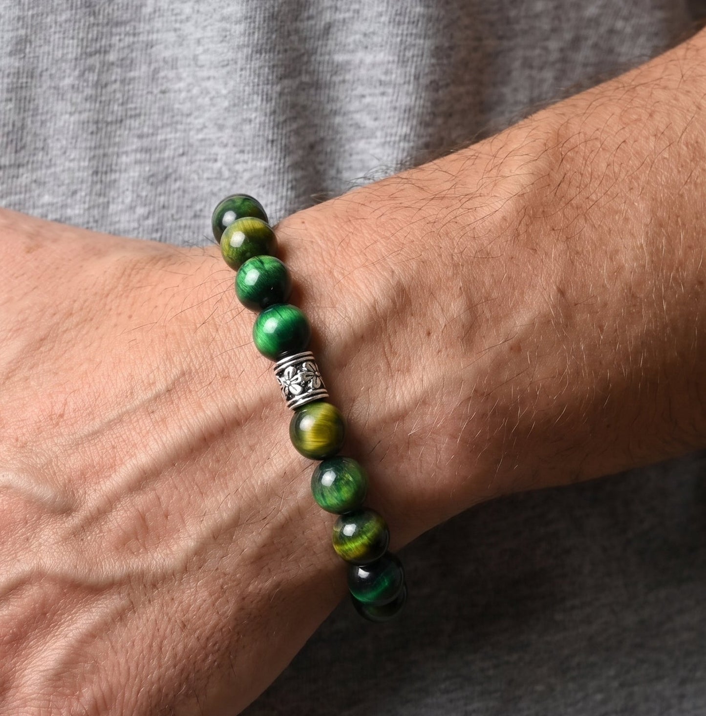 Green tiger's eye bracelet on wrist with silver-toned, engraved clasp centerpiece.