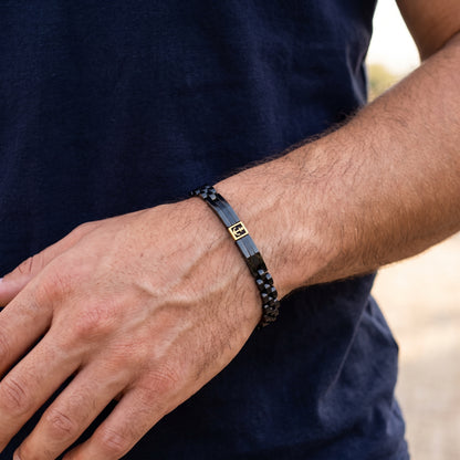Men's black beaded bracelet with gold anchor plate, worn on forearm
