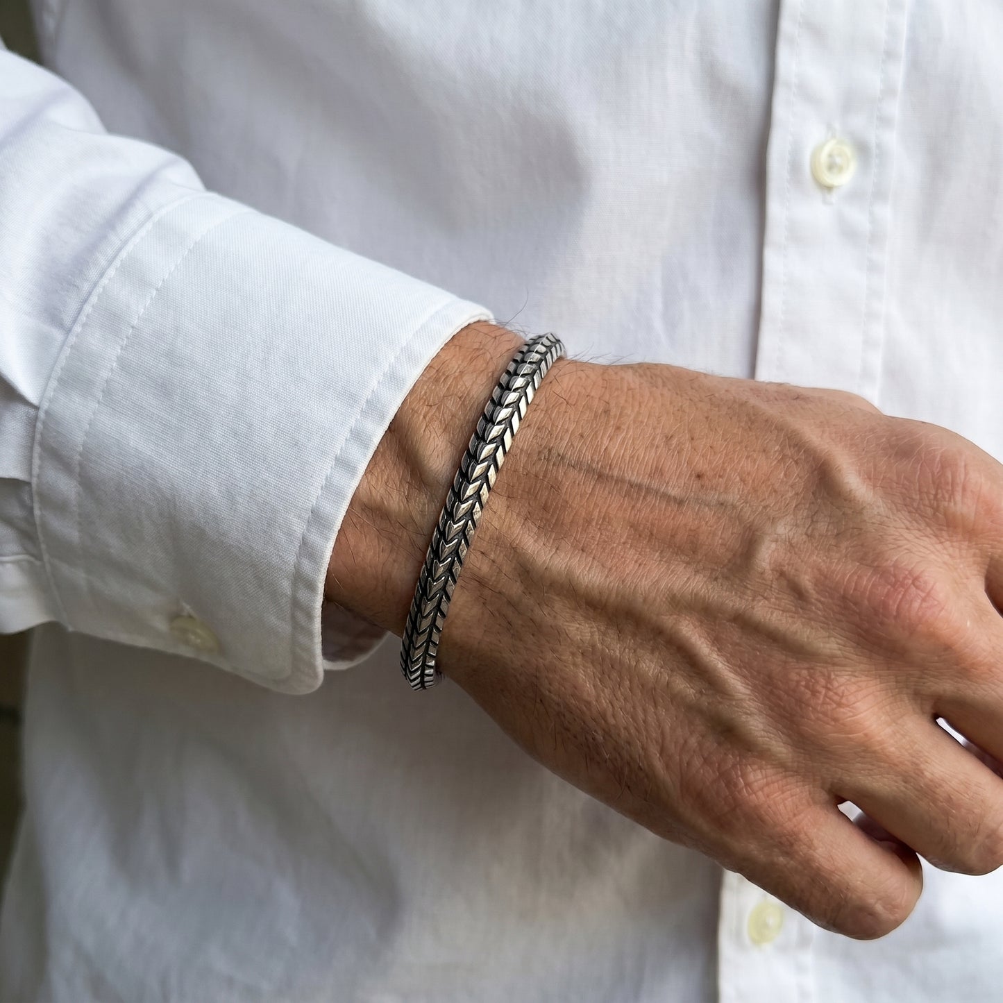 Silver stainless steel braided cuff bracelet on wrist, close-up detail.