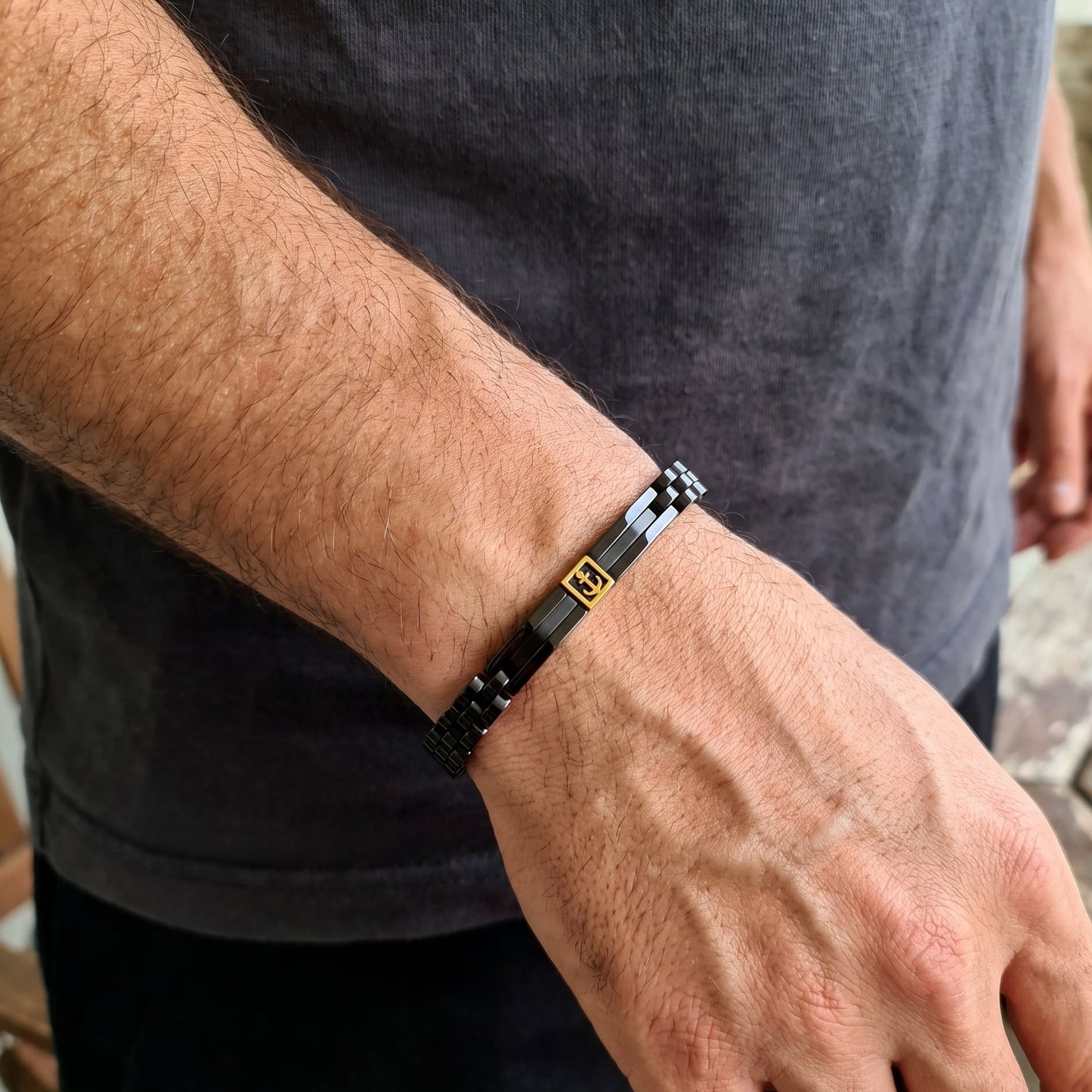 Men's black metal link bracelet with gold anchor inlay, worn on wrist