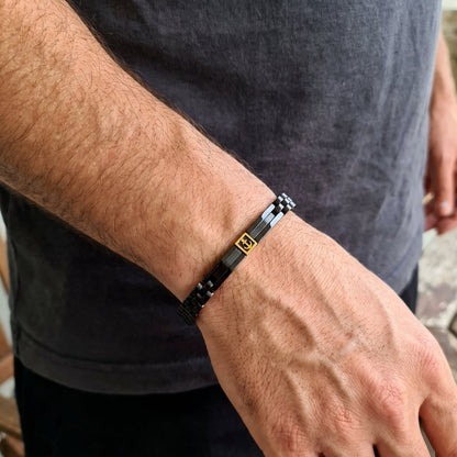 Men's black metal link bracelet with gold anchor inlay, worn on wrist