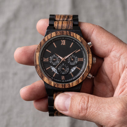 Men's zebrawood and ebony wood wristwatch held in hand, black dial with rose-gold hands and subdials, Overpowered Accessories