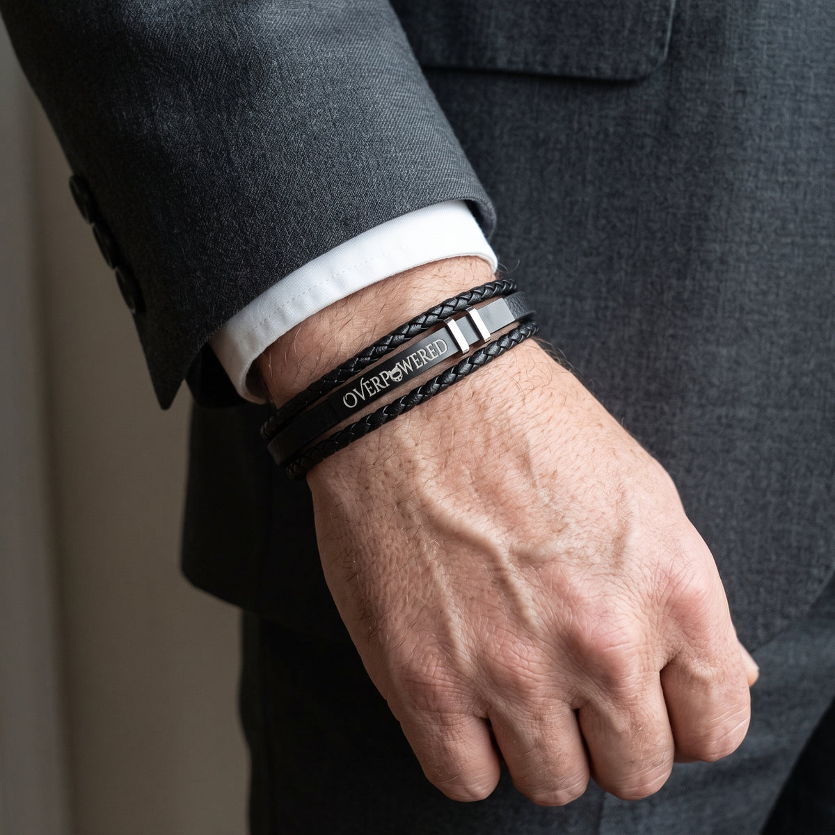 Black leather cuff bracelet with layered bands and 'OVERPOWERED' engraved plate.