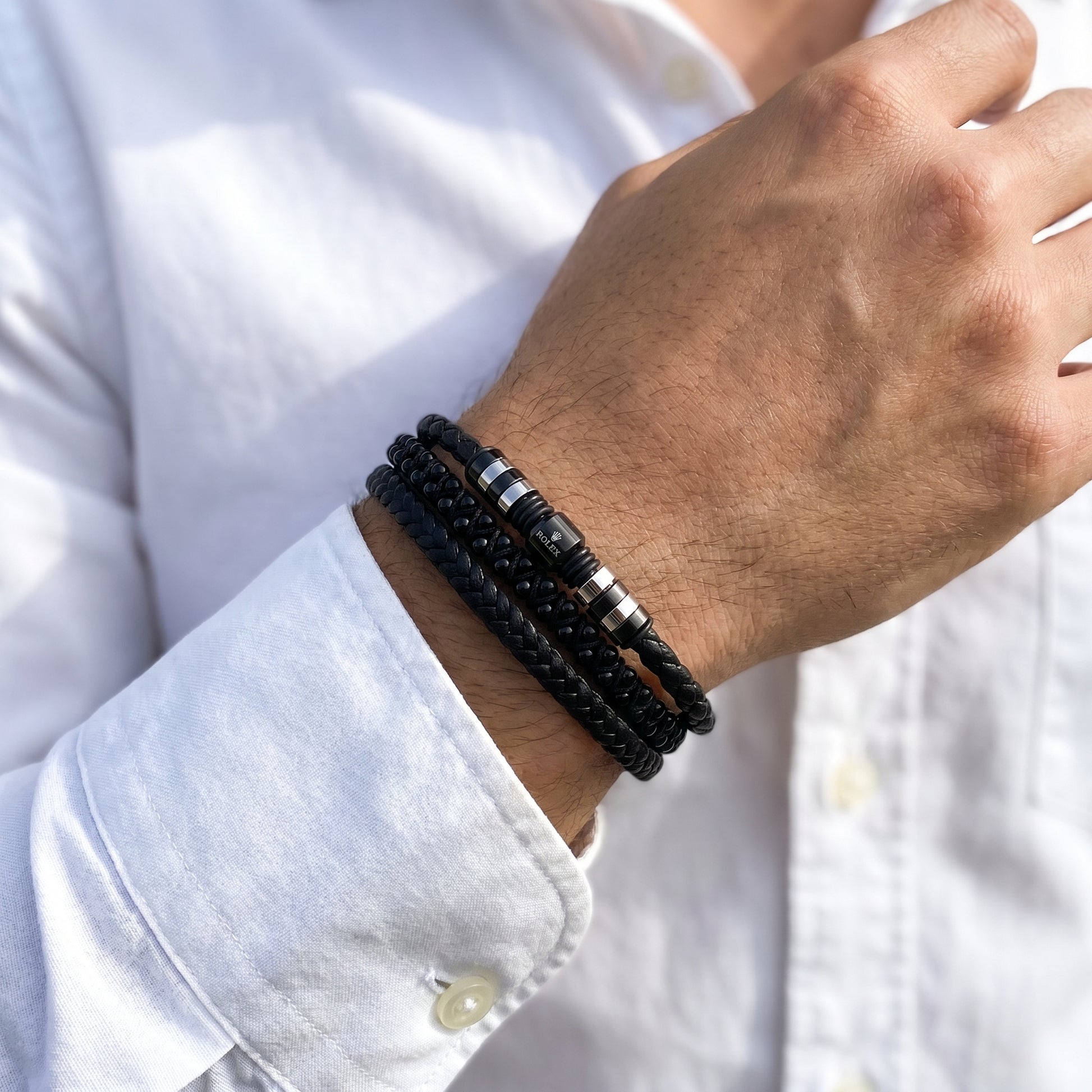 Men's black braided leather bracelet on wrist with striped metal bead accents