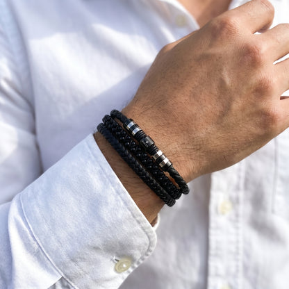 Men's black braided leather bracelet on wrist with striped metal bead accents