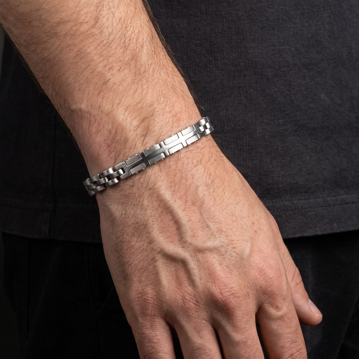 Silver stainless steel link bracelet with checker and cross pattern, worn on wrist