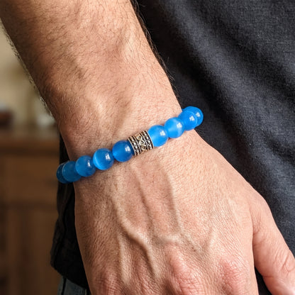 Blue agate bead bracelet on hand, dark engraved metal center detail.