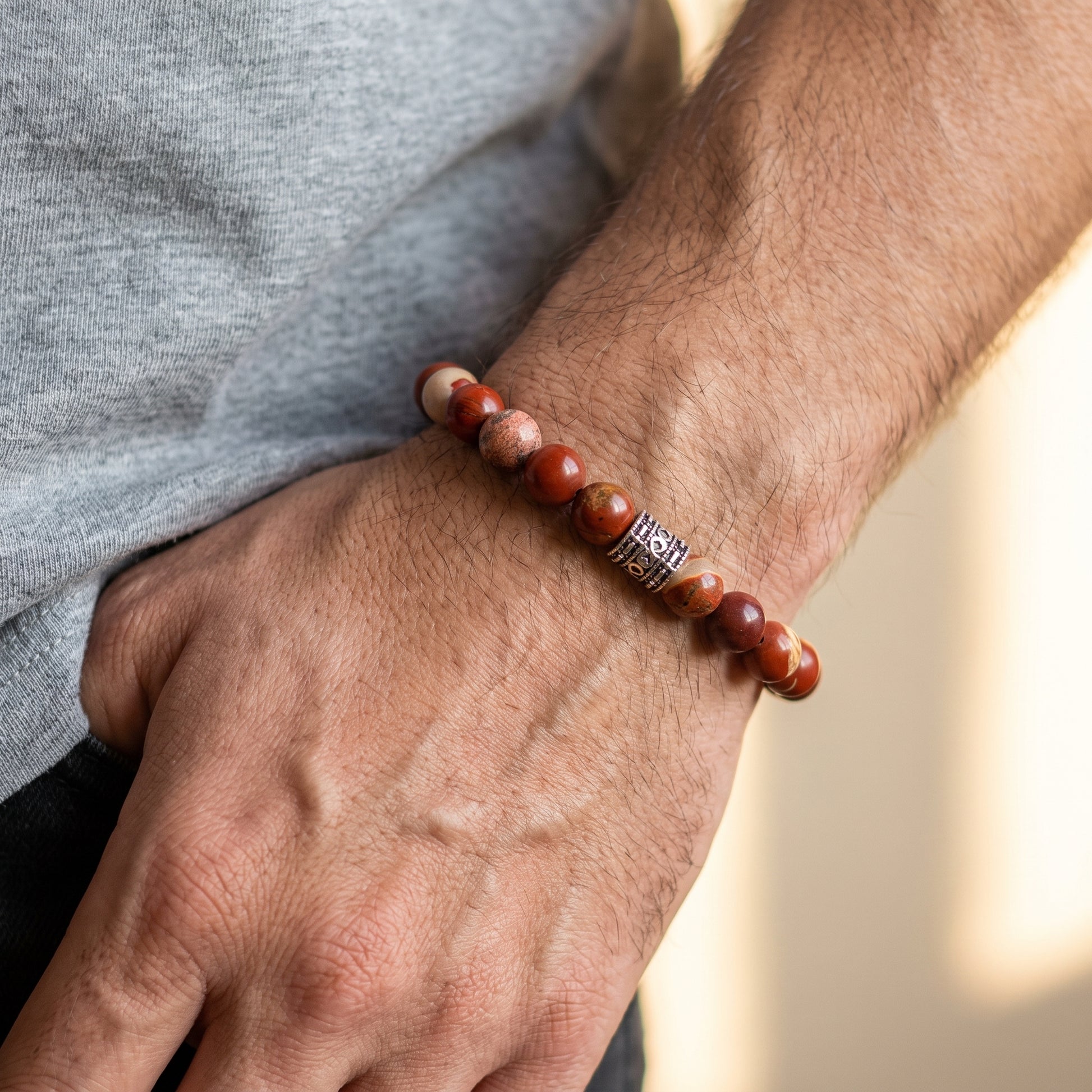 Red jasper stone bracelet on forearm with mixed red beads and silver-tone clasp detail