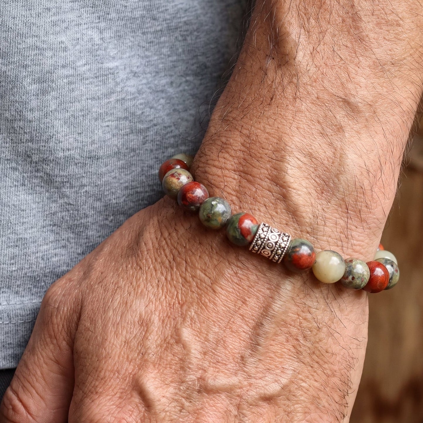 Men's natural stone beaded bracelet on wrist with red, cream, and gray beads and decorative band