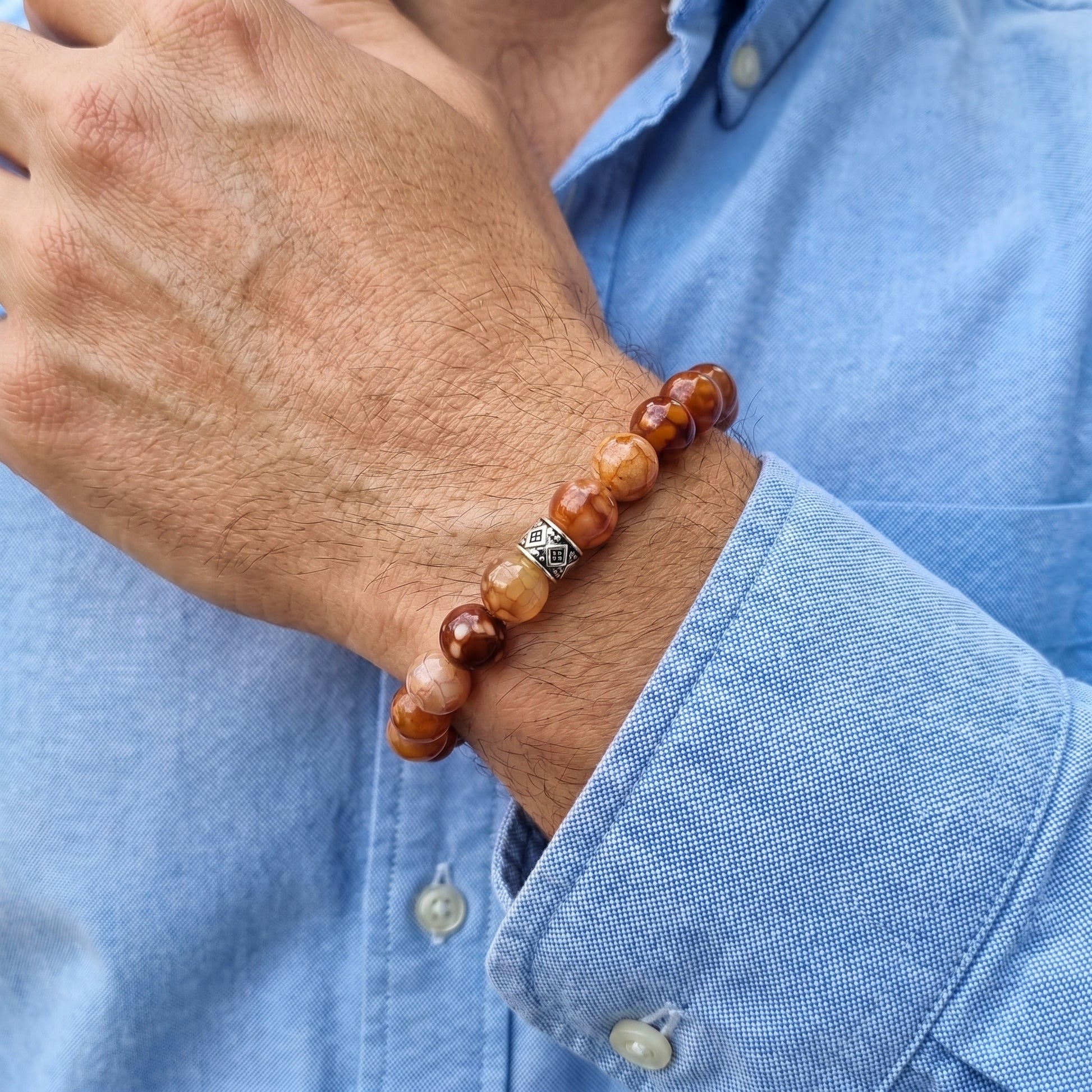 Men's brown stone bead bracelet worn on wrist with silver patterned spacer detail