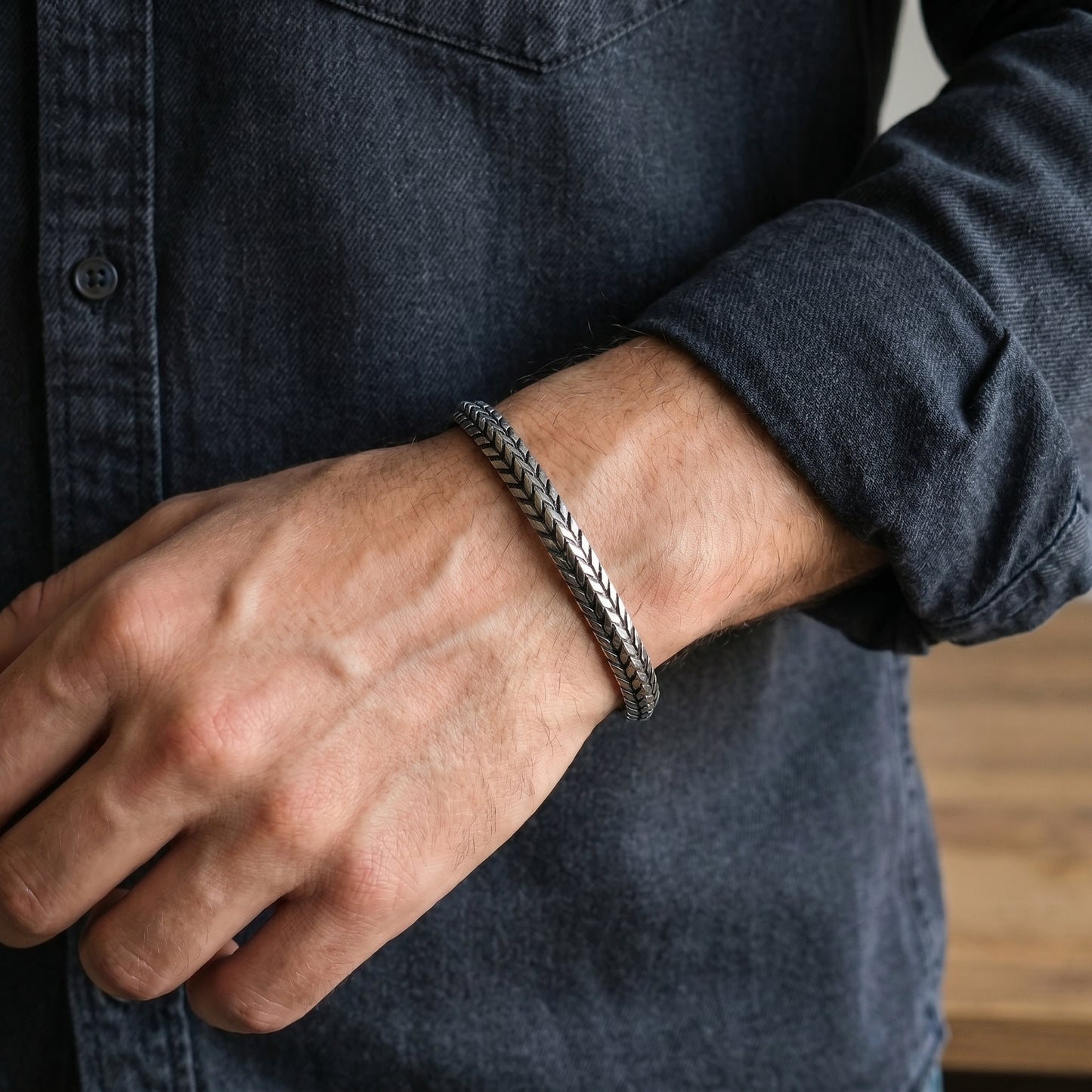 Silver stainless steel braided cuff bracelet on forearm, close-up with hands.
