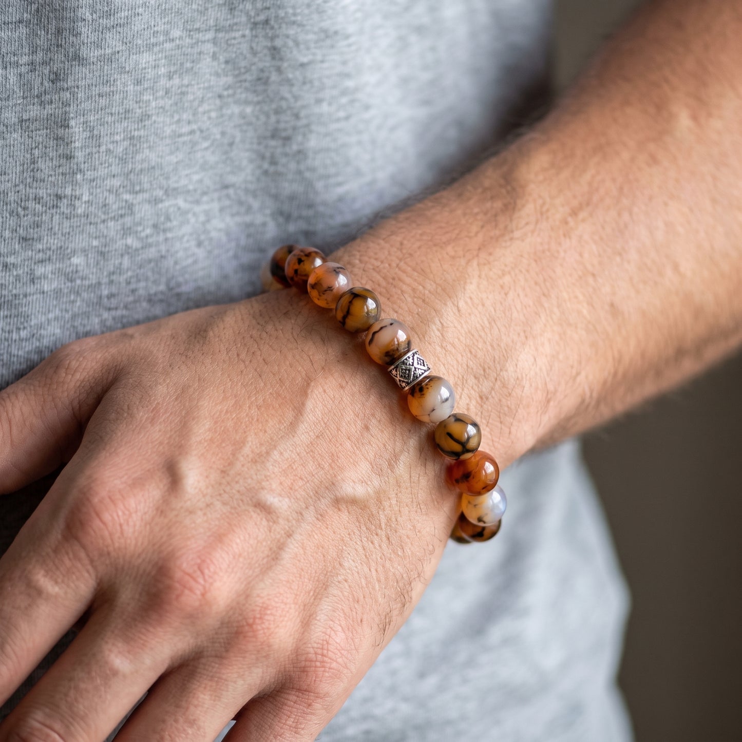 Agate stone beaded bracelet worn on wrist with orange, brown, and white beads and silver centerpiece