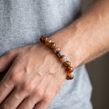 Agate stone beaded bracelet worn on wrist with orange, brown, and white beads and silver centerpiece