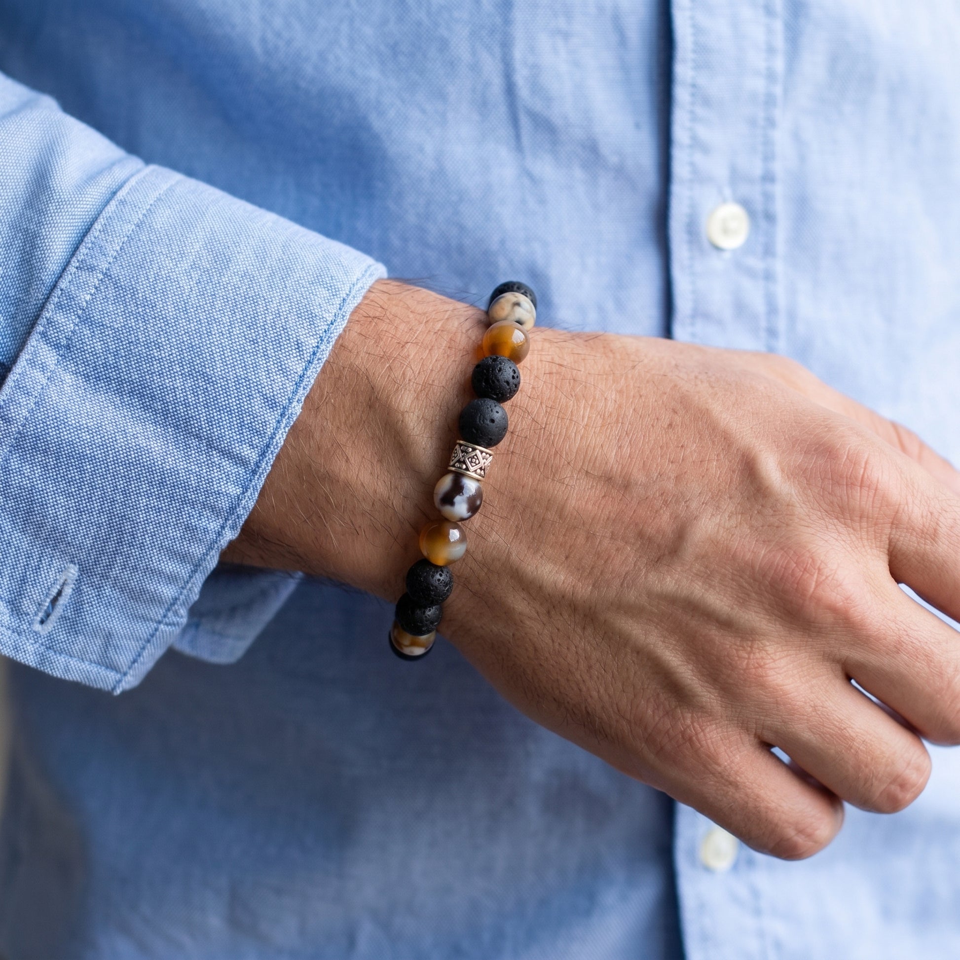Stone bracelet worn on wrist with black lava and orange beads and silver-tone center spacer
