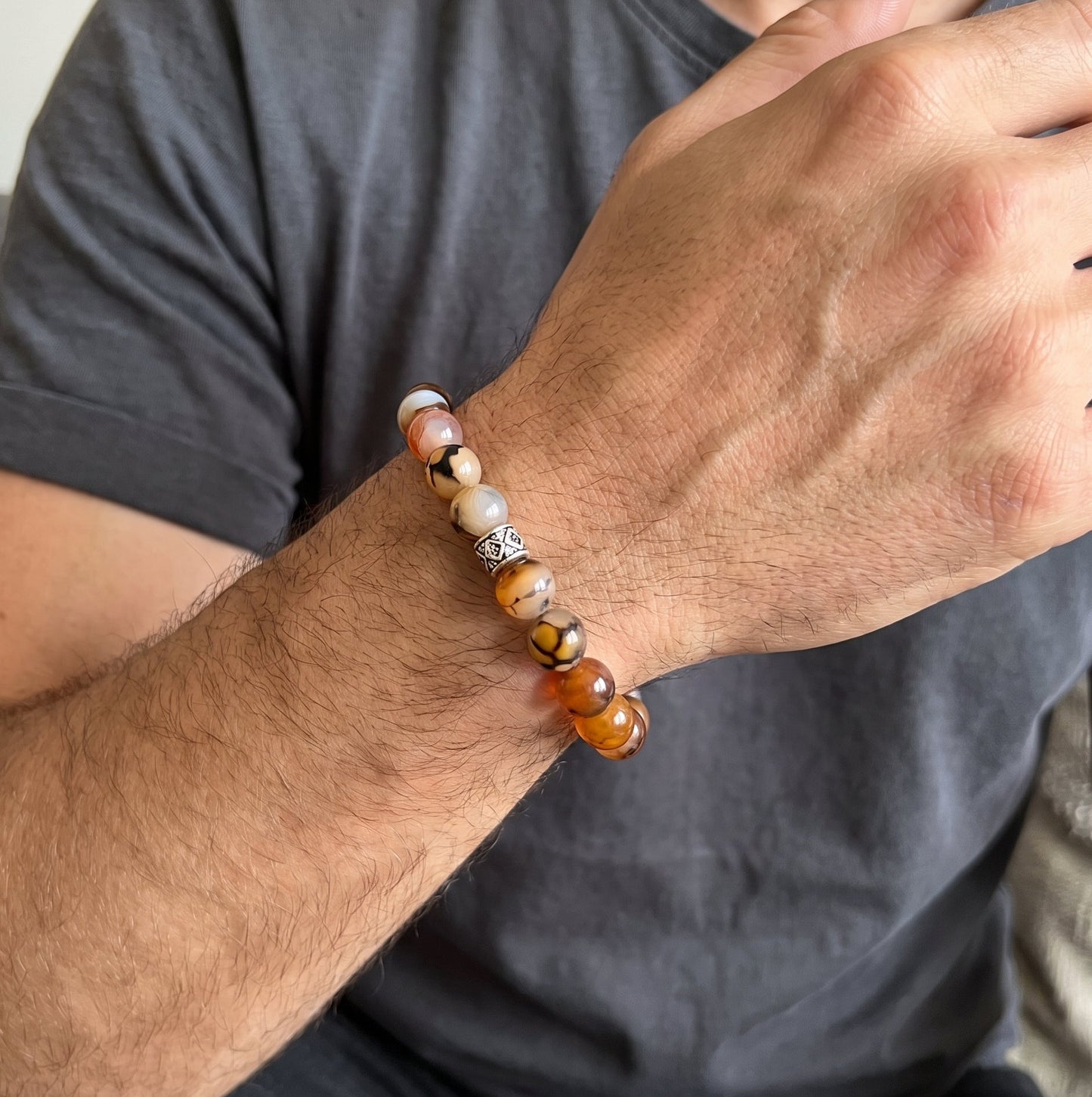 Agate beaded bracelet on a man’s wrist with orange and white stones and a silver geometric charm