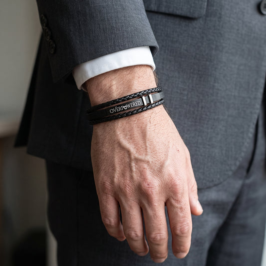 Black leather wrap bracelet with 'OVERPOWERED' metal plate and adjustable clasp.