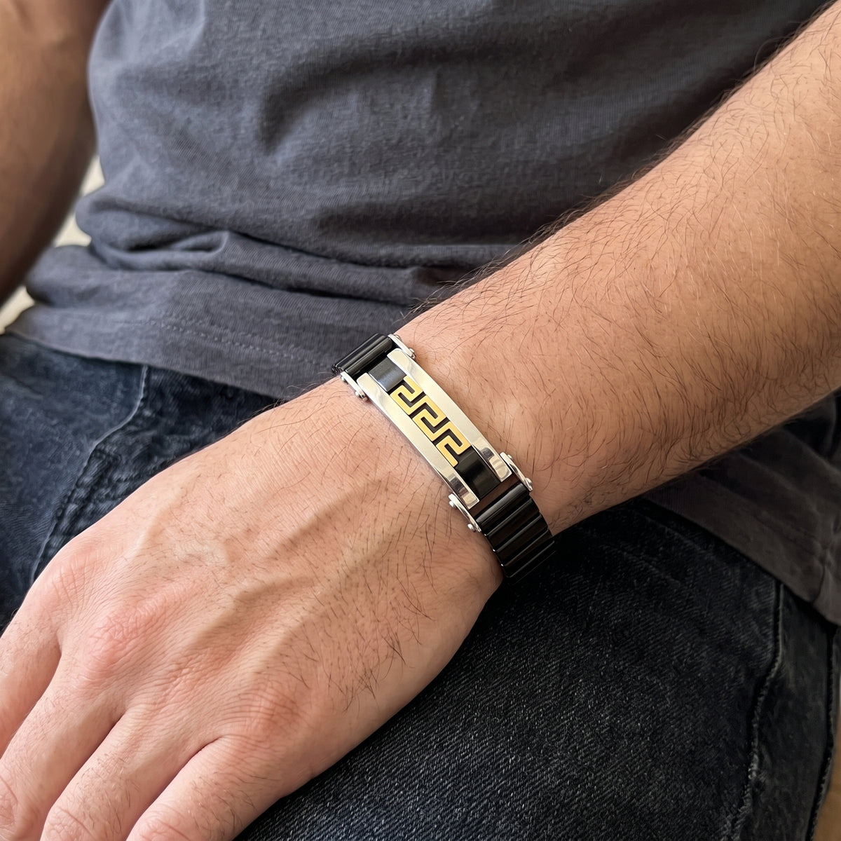 Stainless steel Greek key bracelet with black links and gold trim, silver clasp on wrist