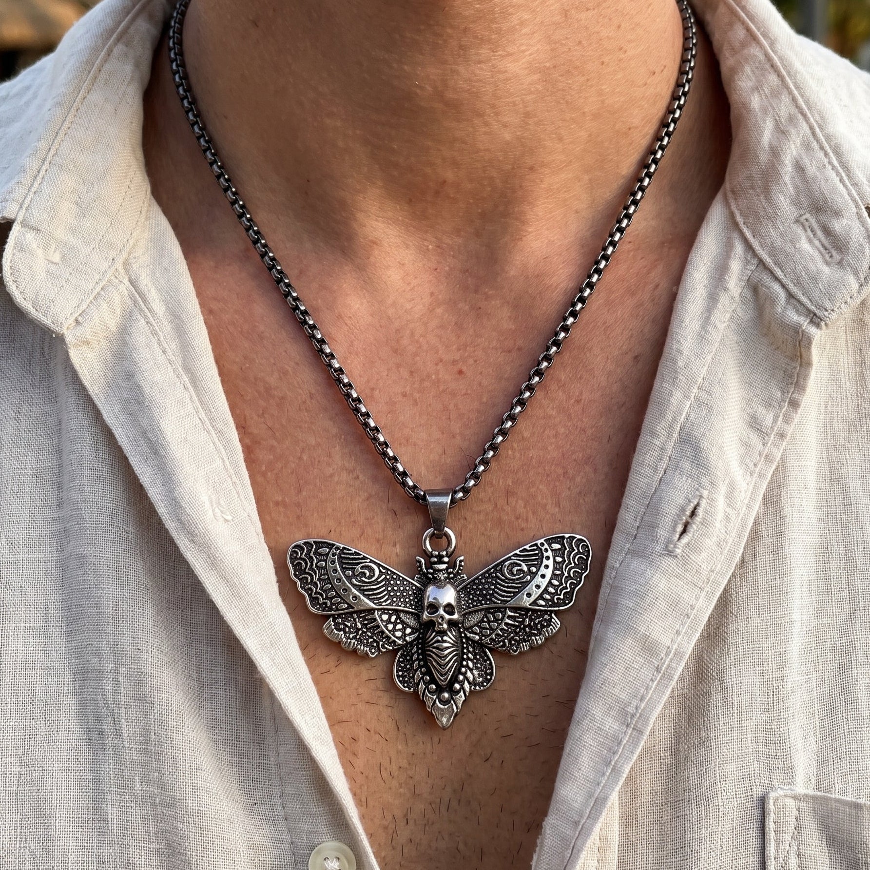 Silver-tone butterfly skull pendant necklace worn on chest over light shirt