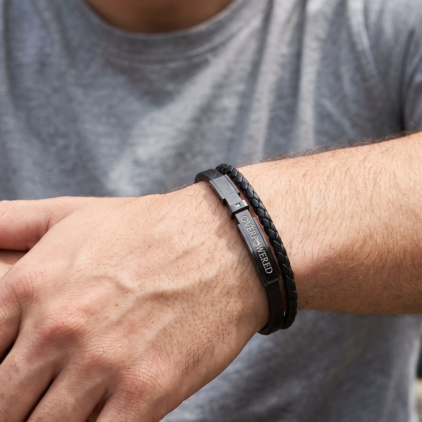 A close-up of a man's wrist wearing a black braided leather bracelet with a silver-toned metal ID tag engraved with 'CZECH REPUBLIC'.