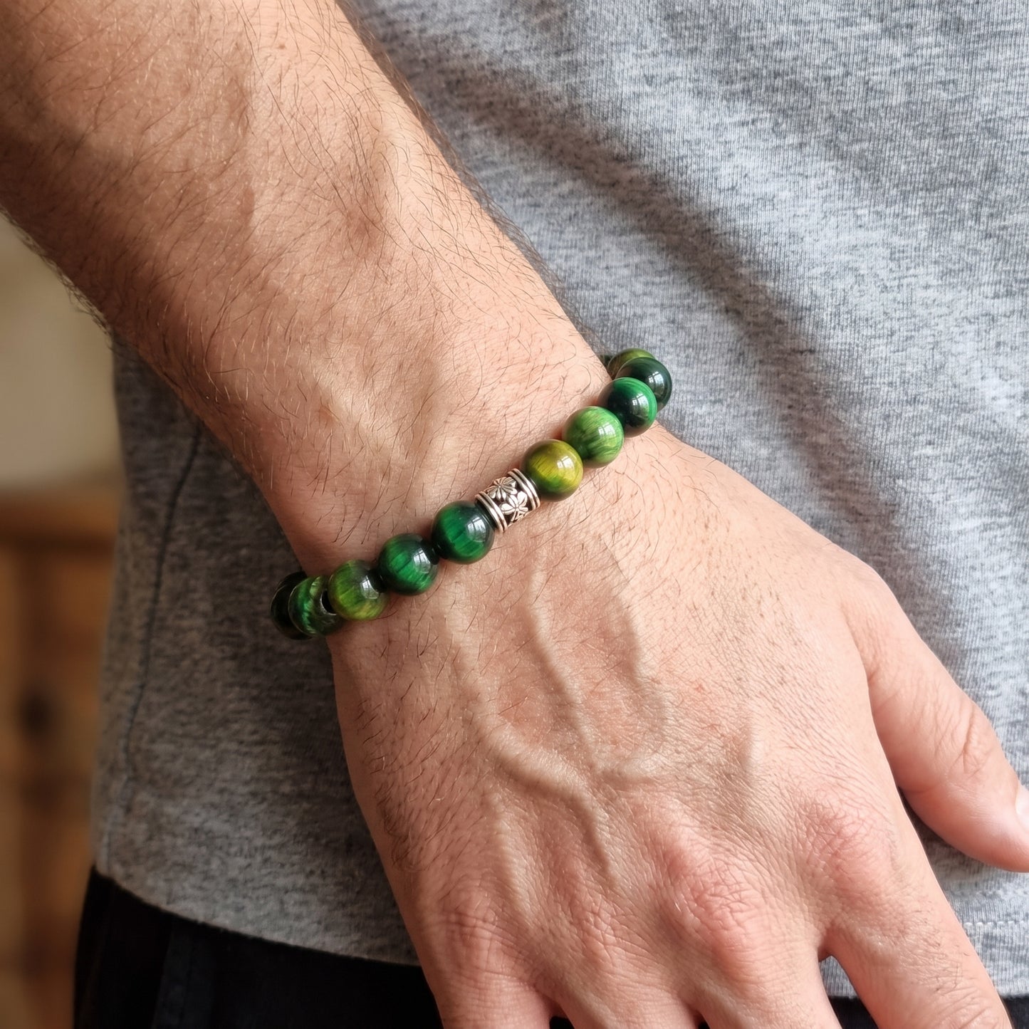 Green tiger's eye stone bead bracelet worn on wrist with silver-toned clasp centerpiece.