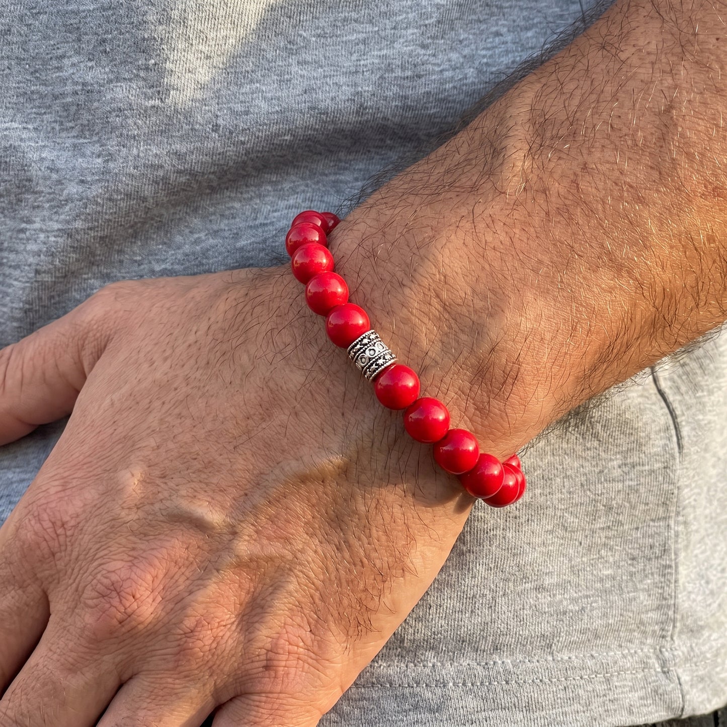 Men's red agate bead bracelet worn on wrist with silver-tone center spacer